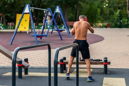 Middle aged caucasian man warms up on the park sport ground. Real athletic shape. Copy space. Preparing for training in the morning. Abandoned park background, early morning.の写真素材