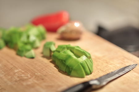 Cut fresh organic avocado, pit, knife and red bell pepper on wooden board in kitchen. Close up, indoors, copy space.の写真素材
