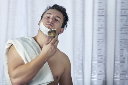 Young handsome caucasian man begins to shave with brush and foam, vintage style of old barber....