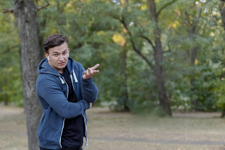 Young handsome caucasian man with perplexed face expression and skeptical gesture at green park,...
