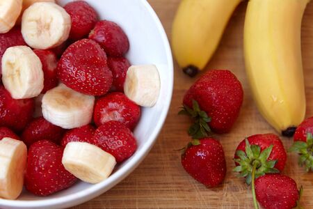 Healthy meal (breakfast), strawberry and bananas. Organic natural diet concept, white plate on wooden desk. Copy space.の写真素材