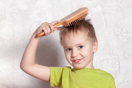 Cute blond caucasian baby boy brushing his hair, smiling. Blue eyes, sly face expression. Indoors, light background, copy space.の写真素材