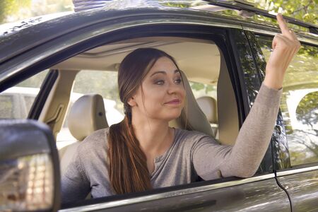 Young attractive caucasian woman shows obscene gesture with middle finger from a car. Strong...