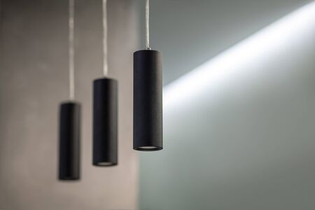 The part of modern loft interior with male design, ascetic minimal background and three lamps in black tubes, hanging from the ceiling. Concrete walls, gray natural colors, indoors, soft selective focus, copy space.の写真素材