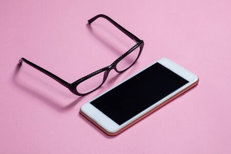 Woman black glasses and mobile phone on bright pink background. Copy space, empty screen for any text. Studioの写真素材