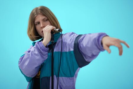 Young handsome caucasian man sings into microphone, posing on blue background with strong emotions and serious face expression. Concept of fun, leisure, party, rock group or karaore vocal. Studio, isolated, copy space.の写真素材