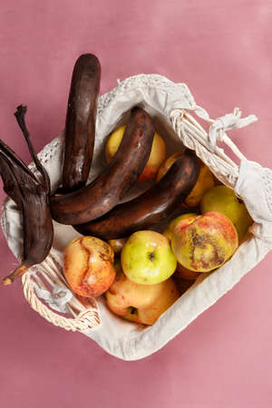 Top view on some overripe fruits in white wicker basket with dirty napkin, tainted bananas,...