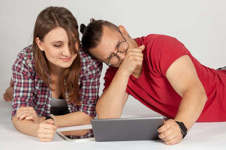 Young couple watching media content online in a tablet lying down and laughing. Wearing casual,...