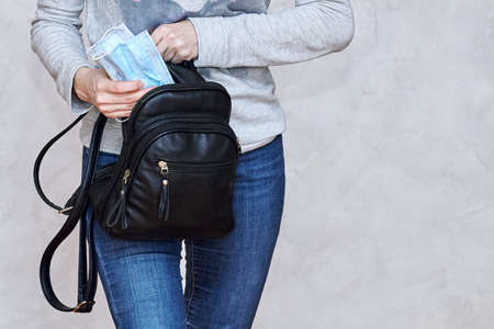 Close up woman hands putting in or taking out some flu masks from black leather backpack on light...
