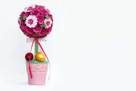 Easter composition with bright flower bouquet in pink pot, decorated by bands and bows, golden and red painted eggs. White background, copy space, big empty place for any text.の写真素材
