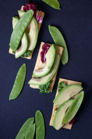 Top view of vegetarian toasts with avocado, green peas and salad, on dark navy blue background. Copy space.の写真素材