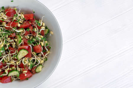 Salad with vegetables and microgreens, sprouts of cereals and green plants of broccoli, tomatoes, cucumbers, oil, salt, pepper in white bowl on light background. Healthy energetic meal. Copy space.の写真素材