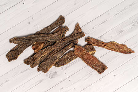 Sliced beef udder cut for pieces, dehydrated and lying down on wooden white background. Homemade natural dry dog treats. Closeup, copy space.の写真素材