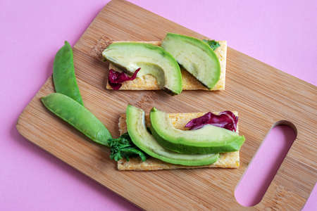 Diet vegetarian toasts with avocado, green peas and salad, on wooden cutting board from ecologic...