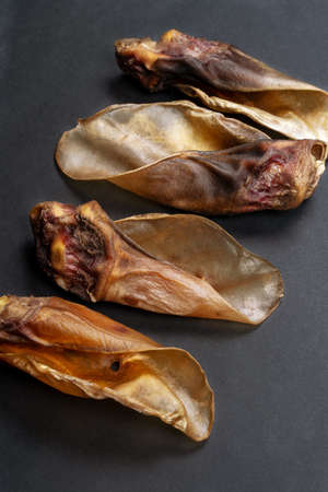 Some dehydrated organic beef ears made for dogs lying down on black background. Homemade meat pet treats, dry chew jerky. Closeup, copy space.の写真素材