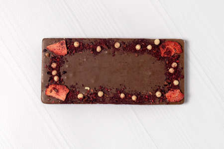 Craft homemade chocolate bar laying down on wooden white background, with pieces of nuts, fruits and...