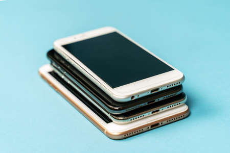 Pile of used old models of mobile phones, black and white, lying down on blue background. copyspace.の写真素材