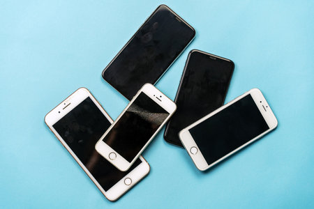 ROSTOV-ON-DON, ROSTOV REGION, RUSSIA - Dec.16 2021: Pile of used old models of mobile phones, black and white, lying down on blue background. Dirty finger spots, broken screen. copyspace.のeditorial素材