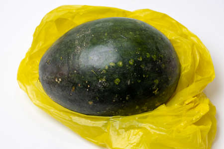 A whole green organic watermelon inside of a yellow poly bag isolated on white background