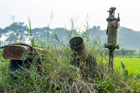 Rusty useless water pump in the agriculture field inside the wild grasses