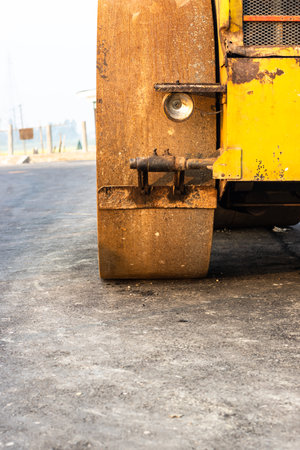 Old rusty wheel of a yellow road roller on the newly constructed road close view