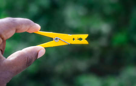 Yellow color cloth hanging clip holding with two fingers close up