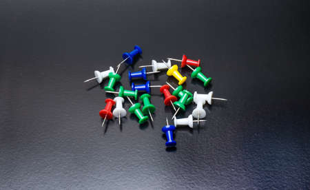 A bunch of colorful paper push pins or thumbtacks on bright dark rough background