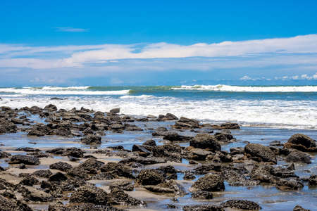 A rocky stone beach with waves under the bright blue skyの写真素材