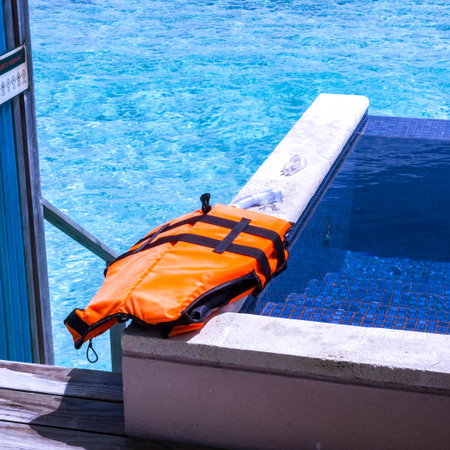Life jacket on the edge of a swimming pool, blue water in the backgroundの写真素材