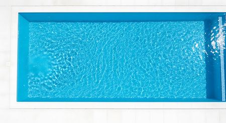 Aerial view of swimming pool. Blue water in rectangular pool. Clean white tiling background. Outdoor leisure activity.の素材