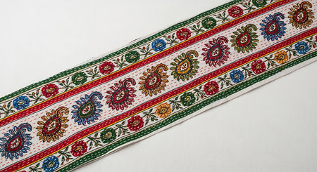Vibrant traditional textile runner with paisley and floral motifs. Kantha embroidery stitches and colorful thread on white fabric create decorative piece. Handcrafted textile art with intricate patterns and bright hues.の素材