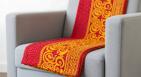 Vibrant red and gold fabric elegantly draped over modern gray armchair close-up. Intricate stitching patterns and rich textures highlight eye-catching design. Textile's vivid colors create visual appeal, enhancing room's aesthetic. Comfortable furniture accent piece adds touch of sophistication to interior.の素材