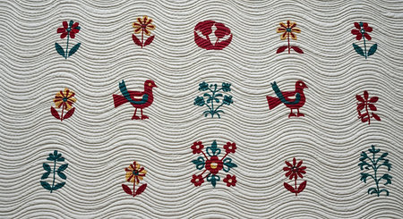 Array of colorful embroidered flowers and birds. These motifs are neatly arranged in rows on a cream-colored quilted textile, featuring distinctive wavy stitching. This showcases intricate textile artistry, combining vibrant elements with traditional quilting techniques.の素材