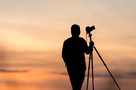 photographer silhouette with accessories and holding hand on tripod ,taking pictures of the beautiful moments during the sunset ,sunriseの写真素材