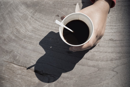 Female hands holding a cup of coffee  on wooden table, top viewの写真素材