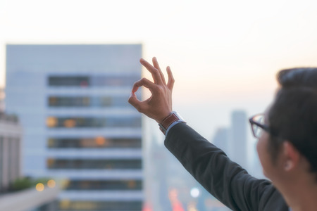 OK hand sign showing by businessman with cityscape  on modern building in Business district at Bangkok city background, Symbols conceptの写真素材