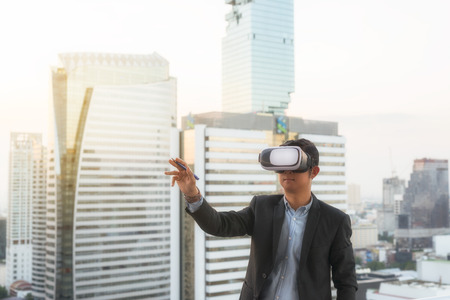 Businessman wearing virtual reality goggles.  background Bangkok modern office buildings, condominium in Bangkok city downtown with sunset sky , Bangkok , Thailandの写真素材