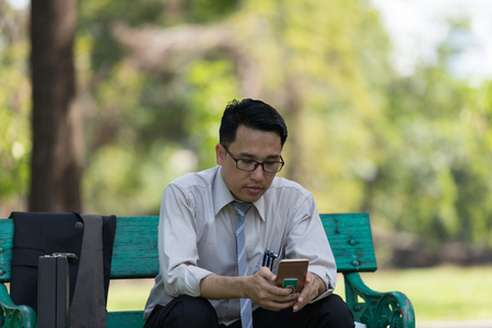 Business man sit check email on  mobile phone at the Park  on the way back home.の写真素材