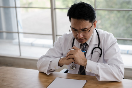 Doctor sitting at desk, worried, thinking hard. To treat patientsの写真素材