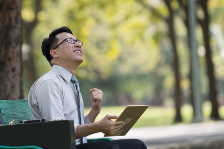 Young businessman looking at digital tablet in the park. He showing signs of rejoicing at their success. A successful businessman conceptの写真素材