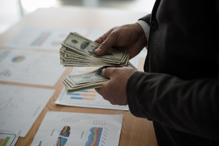 Young asian businessman standing count a dollar bill from his desk. The concept of business resultsの写真素材