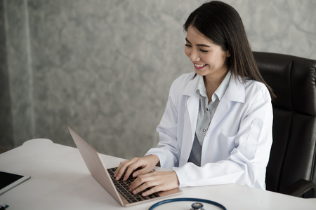 Doctor smiling Asian woman working on a laptop.の写真素材