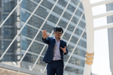 Young Asian businessman in a suit wear and virtual reality glasses who trying to touch something...