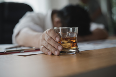 Stressed asian businessman holding a glass of whiskey he sleeping and Data Charts,business document at office desk.  alcohol addiction - drunk businessman conceptの写真素材