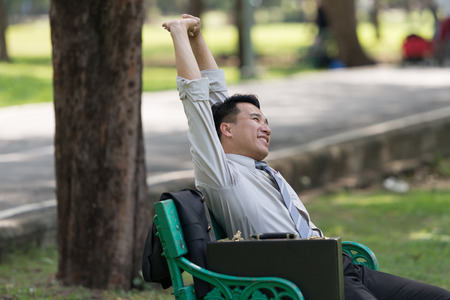 Asian business man relaxing in the park after work. enjoying the shadow of the tree in a sunny day. businessman relieving, rest time conceptの写真素材