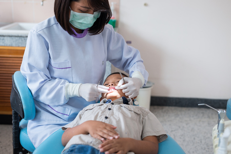 Dentist holding a dental tool. Checking the teeth to the boy lying in the dental chair in a hospital.の写真素材