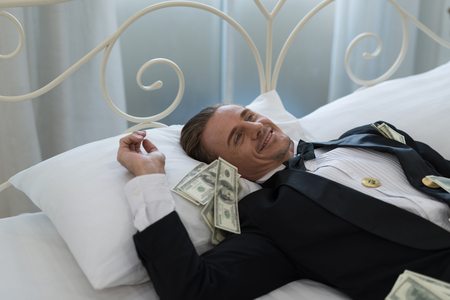 Young Businessman with happy, smile on the bed. who are successful in business and many banknote dollars money. business success conceptの写真素材