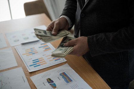 Young asian businessman standing count a dollar bill from his desk. The concept of business resultsの写真素材