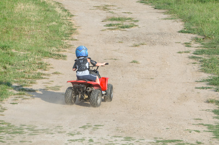 Boy Riding a Red ATV Quad Bike on a Dry Dirt Road on a Summer Dayの写真素材