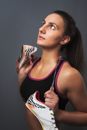 Young Beautiful Sporty Woman Posing with Sprinter Shoes on Gray Backgroundの写真素材